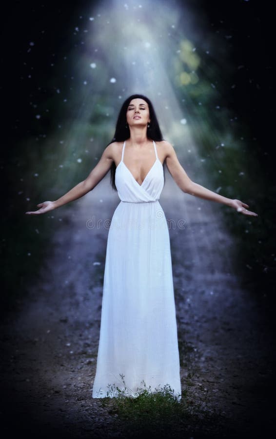 Reizende junge Dame, die ein elegantes langes weißes Kleid genießt die Strahlen des himmlischen Lichtes auf ihrem Gesicht in verz