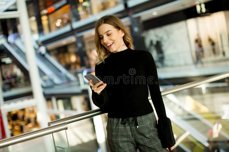 Reizende junge Frau, die am Handy im Einkaufszentrum schaut stockfotografie Reizende junge Frau, die am Handy im Einkaufszentrum schaut stockfotografie