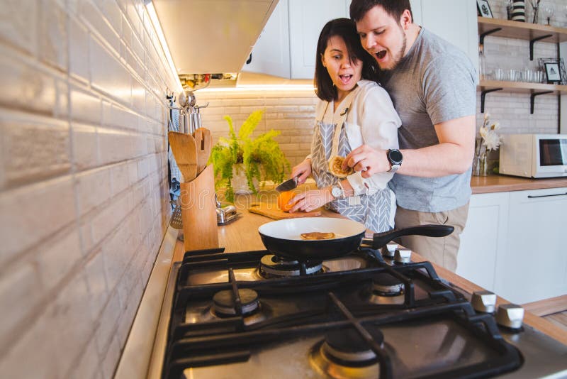 Reizende Paare, die auf der Küche beim Kochen des Frühstücks umarmen lizenzfreie stockfotografie Reizende Paare, die auf der Küche beim Kochen des Frühstücks umarmen lizenzfreie stockfotografie