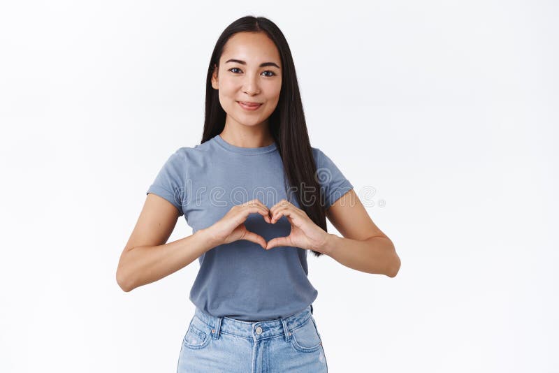 Reizendes, freundlich-aussehendes zartes asiatisches Mädchen, in der Liebe zu bekennen, das Showherzzeichen und Lächeln, die dumm lizenzfreies stockbild