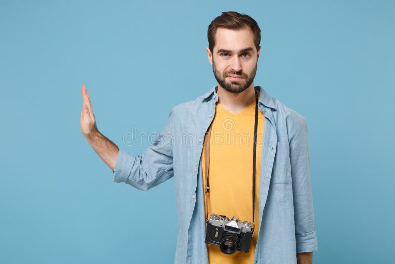 Traveler tourist man in yellow clothes with photo camera isolated on blue background. Male passenger traveling abroad on weekends. Air flight journey concept. Showing stop gesture aside with palm. Traveler tourist man in yellow clothes with photo camera isolated on blue background. Male passenger traveling abroad on weekends. Air flight journey concept. Showing stop gesture aside with palm