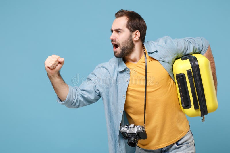 Traveler tourist man in casual clothes with photo camera isolated on blue background. Male passenger travele abroad on weekends. Air flight journey concept. Holding suitcase clenching fist running. Traveler tourist man in casual clothes with photo camera isolated on blue background. Male passenger travele abroad on weekends. Air flight journey concept. Holding suitcase clenching fist running