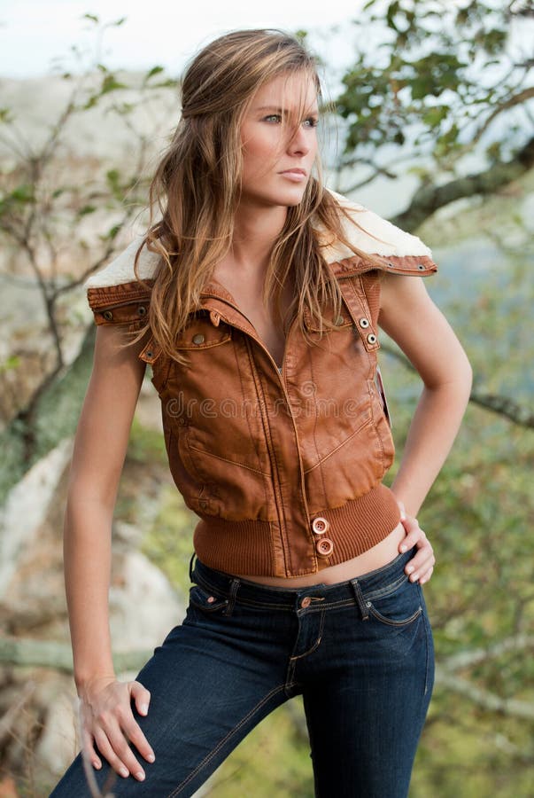 A portrait of an attractive young woman standing on a mountaintop wearing a leather jacket vest and jeans. A portrait of an attractive young woman standing on a mountaintop wearing a leather jacket vest and jeans