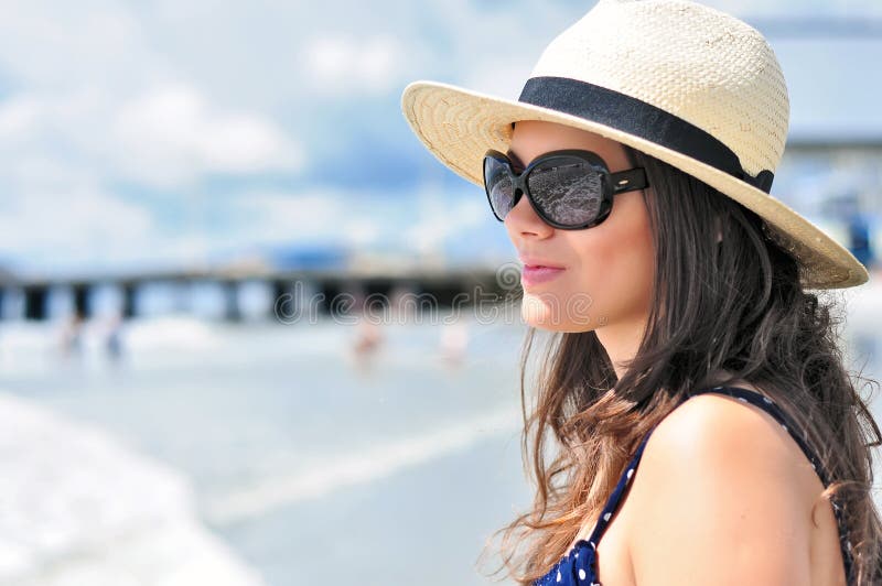 brunette girl with beach hat, summer dress and sunglasses staring in vain with the ocean reflection in her glasses. brunette girl with beach hat, summer dress and sunglasses staring in vain with the ocean reflection in her glasses