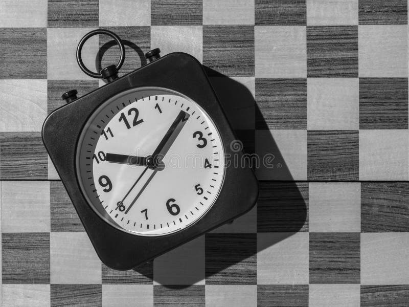 Relógio de xadrez antigo no tabuleiro de xadrez com figuras, bandeira em  posição que indica que o tempo está acabando em fundo escuro