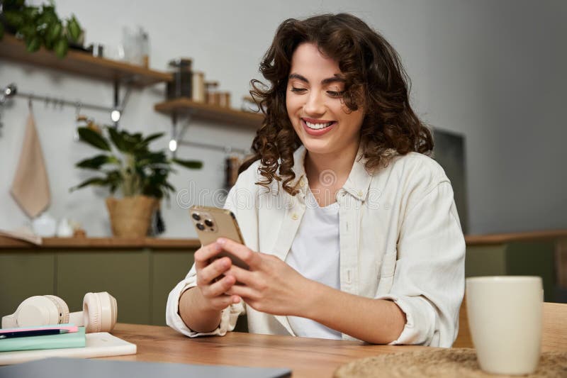 Relajación en casa al comprobar los mensajes. Una bella joven se sienta cómodamente en casa disfrutando su tiempo usando su smartphone con alegría.