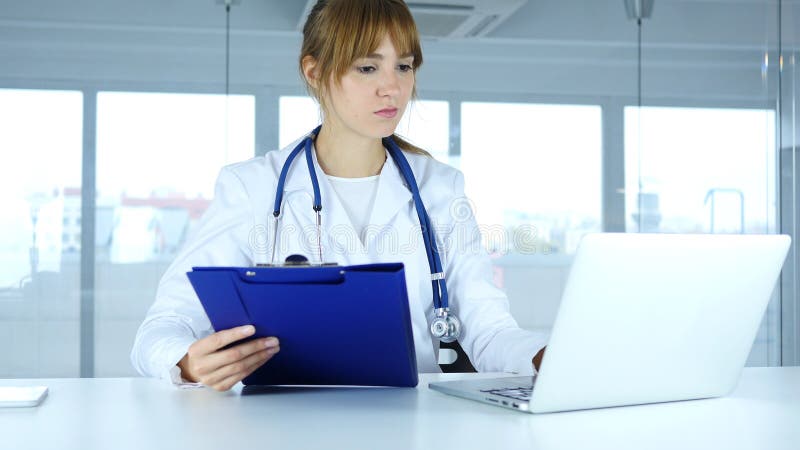 Relatórios médicos de leitura do doutor fêmea novo e trabalho no portátil fotos de stock royalty free Relatórios médicos de leitura do doutor fêmea novo e trabalho no portátil fotos de stock royalty free