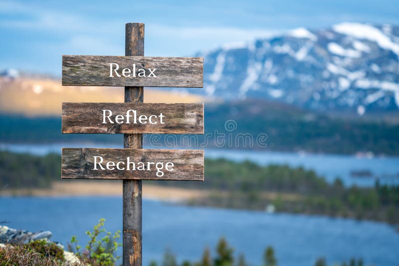 Relax reflect recharge text on wooden signpost outdoors in landscape scenery during blue hour.