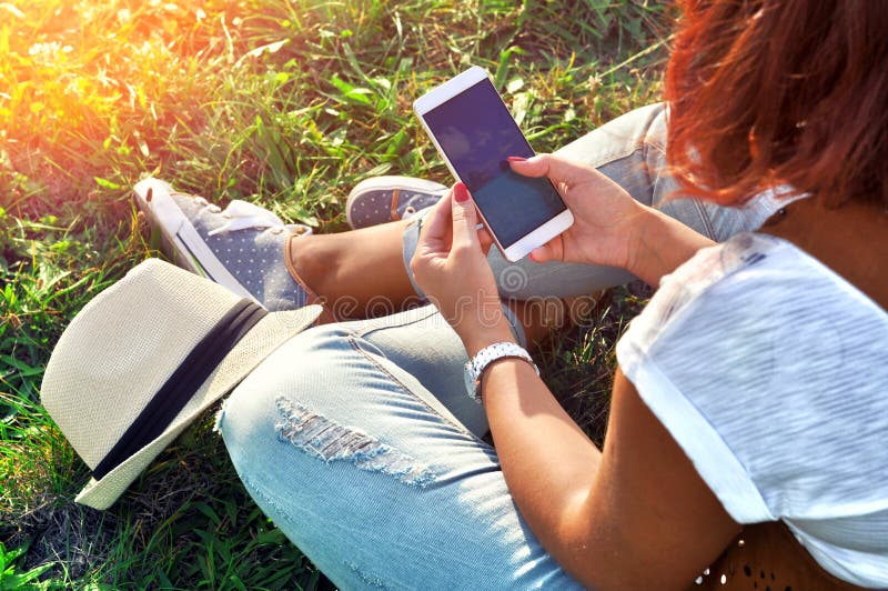 Relaxation avec un mobile Temps de coupure Jeune femme à l'aide du téléphone portable et se reposant sur l'herbe photographie stock Relaxation avec un mobile Temps de coupure Jeune femme à l'aide du téléphone portable et se reposant sur l'herbe photographie stock
