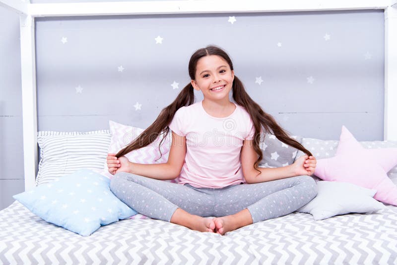 Relaxation and meditation. Girl child sit on bed in her bedroom. Kid prepare to go to bed. Pleasant time for evening
