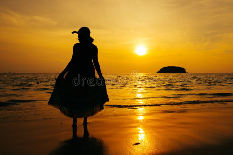 Relaxe a posição da mulher na silhueta do por do sol do mar da praia fotografia de stock Relaxe a posição da mulher na silhueta do por do sol do mar da praia fotografia de stock