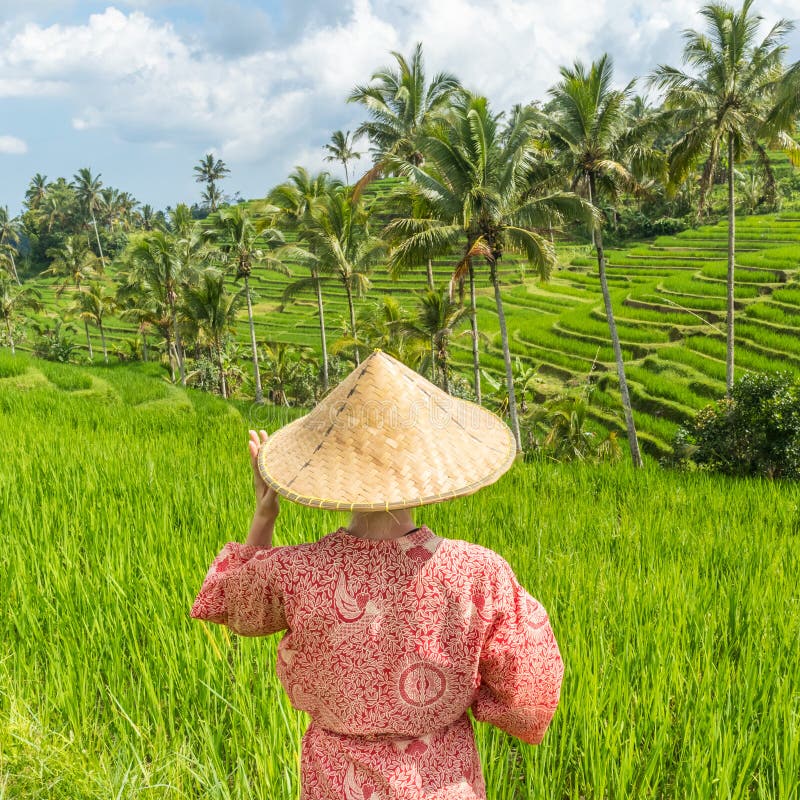 Relaxed fashionable caucasian woman wearing red asian style kimono and traditional asian paddy hat walking amoung