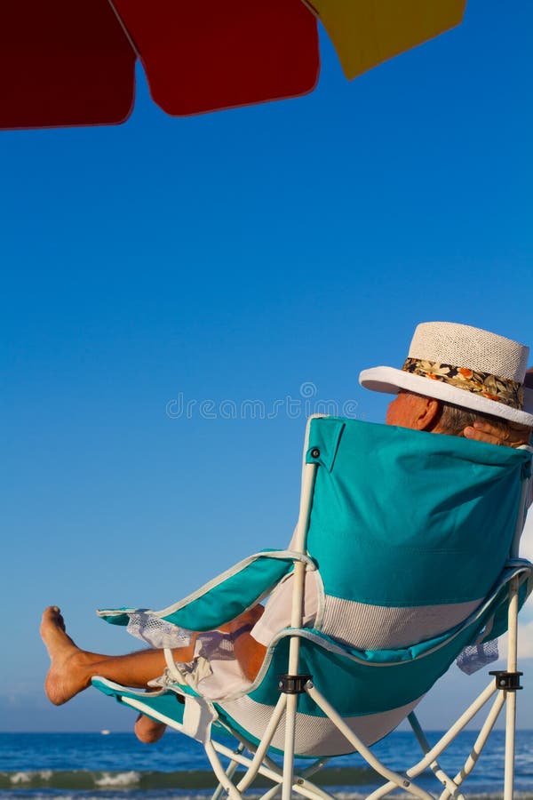 Descuidado hombre descansa sobre el externo sillas en Playa el sol un paraguas.