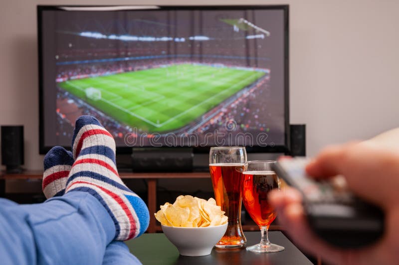 Relaxed man lying on sofa while watching football match on television, beer and chips on table stock image Relaxed man lying on sofa while watching football match on television, beer and chips on table stock image
