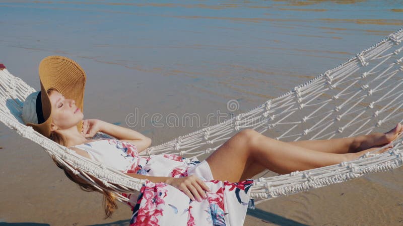 Relaxed woman lounging in hammock at sandy beach by the sea.