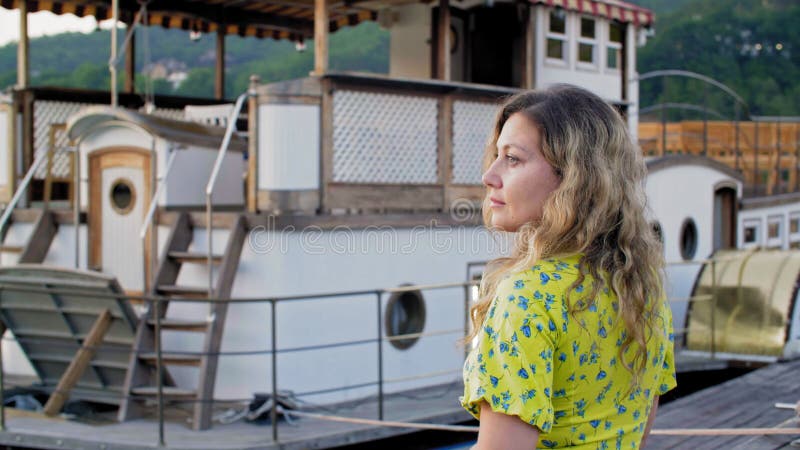 Relaxed woman on sea pier on vintage ship background at summer trip. Tourist woman resting on lake pier half turn on