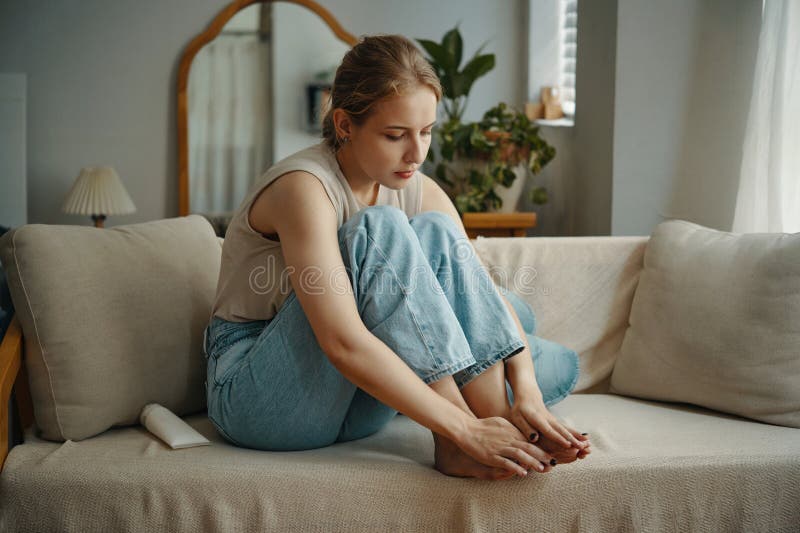 Relaxed Woman Sitting on Sofa Examining Toenails stock image
