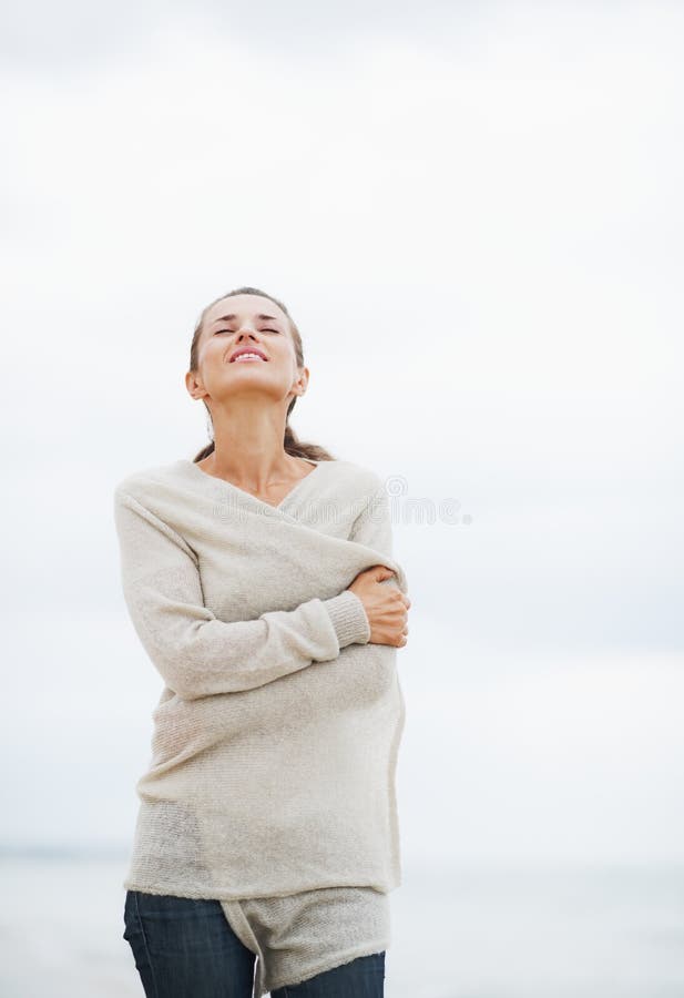 Relaxed young woman in sweater walking on lonely beach