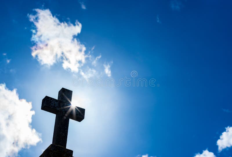 Religious cross, symbol of christianity, against blue cloudy sky with sunbeams
