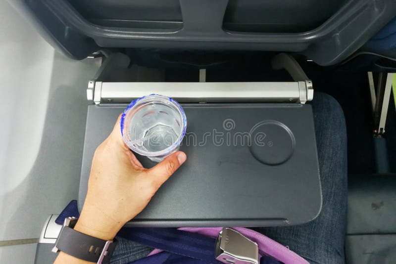 Remettez tenir l'eau minérale jetable sur la table dans l'avion d'air photographie stock libre de droits Remettez tenir l'eau minérale jetable sur la table dans l'avion d'air photographie stock libre de droits