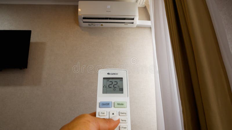 Remote control in hand opposite the air conditioner, which hangs on the wall. royalty free stock photos