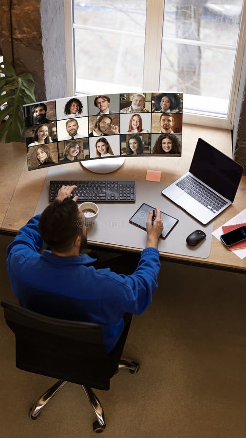 Remote worker in blue sweatshirt using tablet and keyboard while engaged in virtual team meeting displayed on curved royalty free stock photos