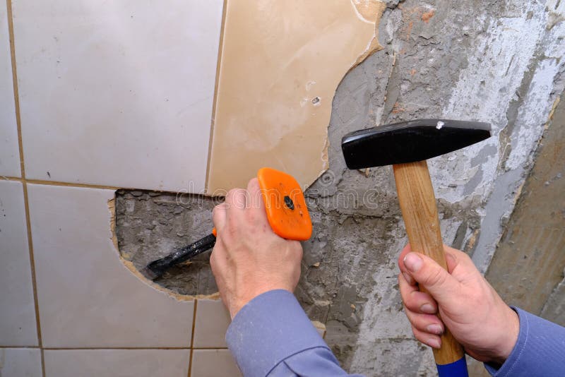 Removing old tiles from the wall in the kitchen using a chisel with a special plastic nozzle for safety when hammering