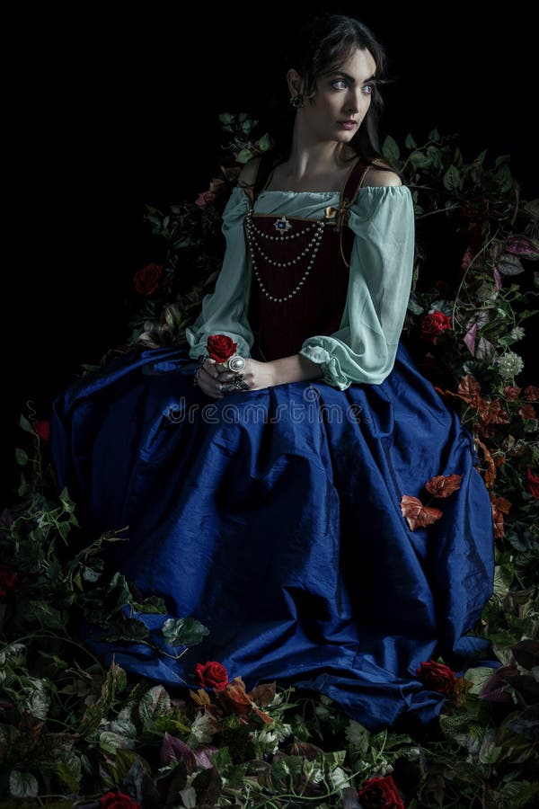 A Renaissance or Fantasy/fairytale/gypsy woman wearing a red brocade corset and blue silk skirt, surrounded with vines, and holding a red rose