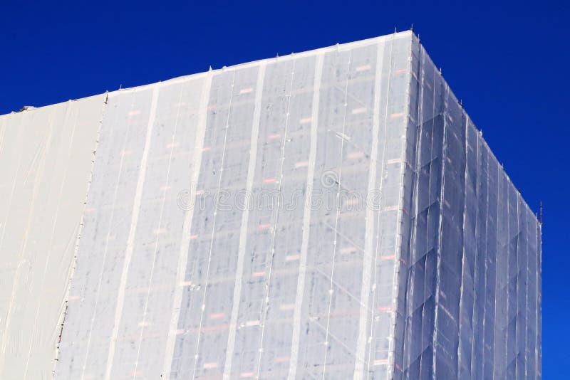 Protective cover assembly for the building during the renovation. Plastic tarpaulin and scaffolding. Works site Covered and wrapped. This is a building of the utmost character that was constructed before the `70s. Background. Protective cover assembly for the building during the renovation. Plastic tarpaulin and scaffolding. Works site Covered and wrapped. This is a building of the utmost character that was constructed before the `70s. Background.