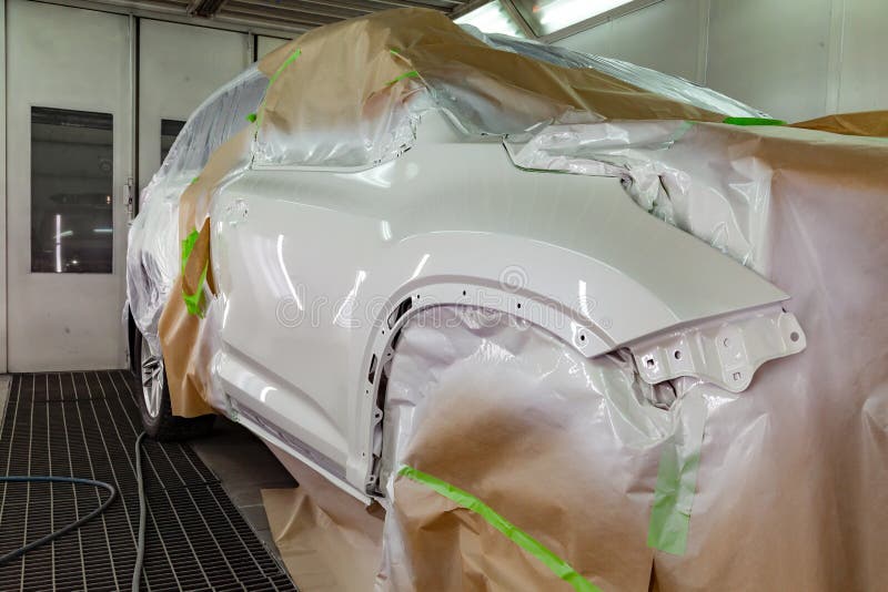 Repainting the damaged front part of an expensive SUV vehicle in white in a professional auto repair shop using paintwork