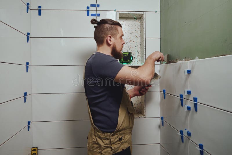 Repairman Applying Tile Adhesive with a Trowel on the Bathroom Wall