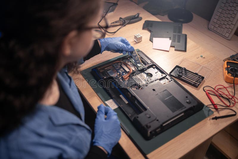 Repairman girl disassembling laptop motherboard and install memory chip. Engineer fixing broken computer at work in old repair shop. Electronic repair shop, technology renovation, business concept