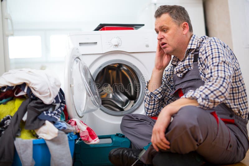 Repairman naprawiania płuczka W kuchni, Siedzi Obok Brudnej pralni fotografia royalty free