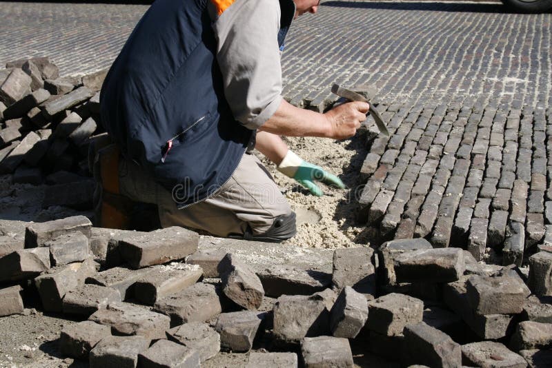 Man with chisel on his knees repairing the brick road. Man with chisel on his knees repairing the brick road