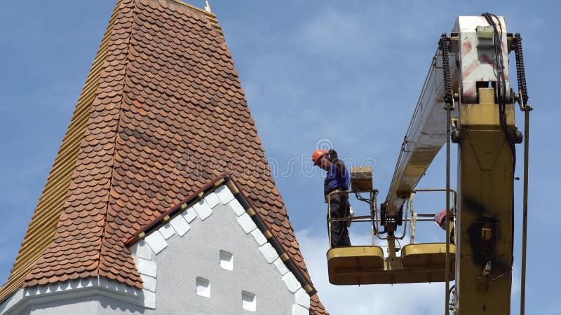 Reparatur und Rekonstruktion des alten Dachs aus roten Fliesen eines Gebäudes. der Arbeiter im Korb eines Krans ist und arbeitet