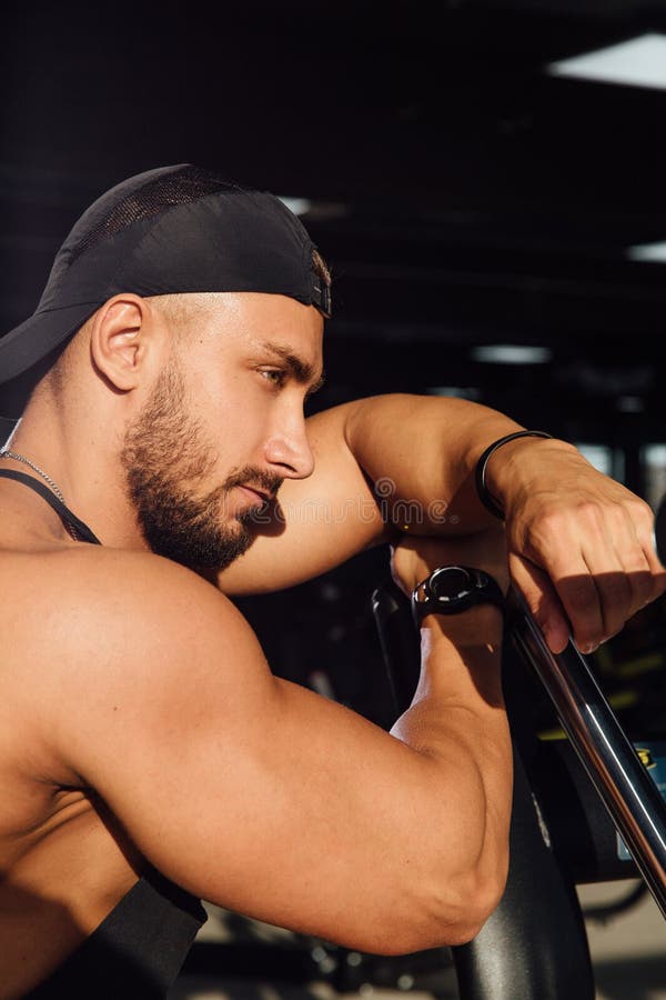 Repos modèle de grande forme physique d'homme fort dans le gymnase penché contre l'équipement de sport de simulateur image libre de droits Repos modèle de grande forme physique d'homme fort dans le gymnase penché contre l'équipement de sport de simulateur image libre de droits