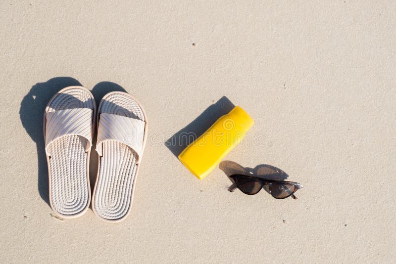 Repos sur la plage : pantoufles, crème protectrice et lunettes de soleil sur le sable propre images libres de droits Repos sur la plage : pantoufles, crème protectrice et lunettes de soleil sur le sable propre images libres de droits