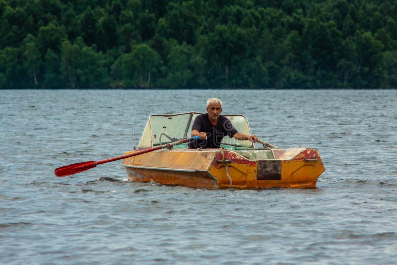 REPUBLIC OF KARELIA, RUSSIA - JULY 2, 2013: Old gray-haired tanned man sailing on boat with paddles on karelian lake