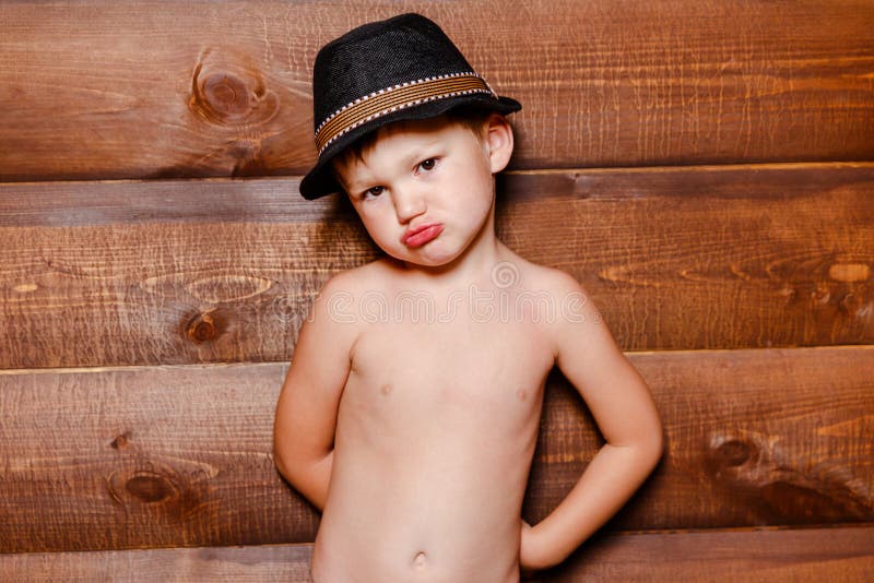 Resentful boy in hat on the background of wooden wall