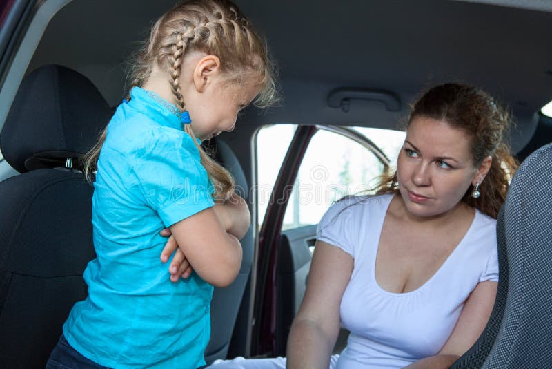 Resentful child refusing get in safety seat under mother severe look