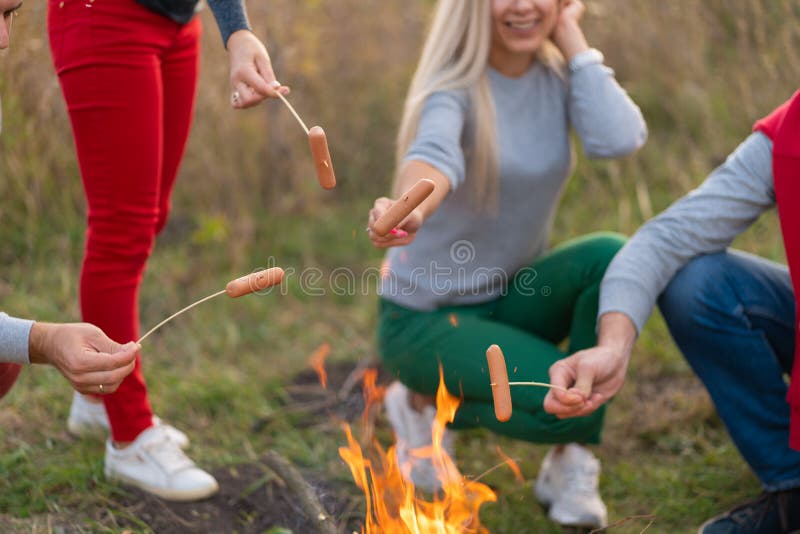 Resor, turism, hike, picknick och människor - grupp av lyckliga vänner som friterar korv på campfire arkivbild Resor, turism, hike, picknick och människor - grupp av lyckliga vänner som friterar korv på campfire arkivbild