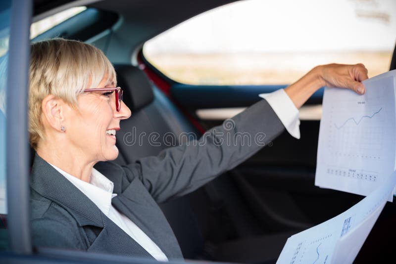Responsabile superiore o donna d'affari soddisfatta che osserva le carte dei rapporti di vendita mentre si trova sul sedile poster immagini stock Responsabile superiore o donna d'affari soddisfatta che osserva le carte dei rapporti di vendita mentre si trova sul sedile poster immagini stock