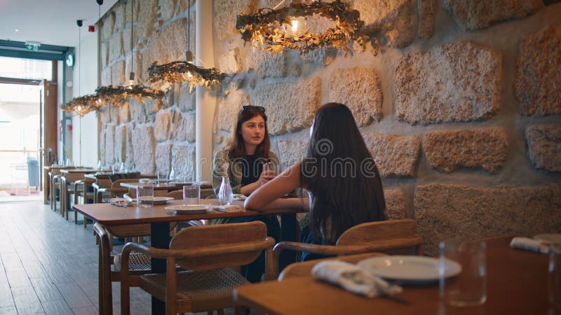 Friendly couple gossiping restaurant enjoying cozy atmosphere. Two beautiful women talking sharing news at weekend meeting in cafeteria. Young girls having lunch together chatting discussing life. Friendly couple gossiping restaurant enjoying cozy atmosphere. Two beautiful women talking sharing news at weekend meeting in cafeteria. Young girls having lunch together chatting discussing life.