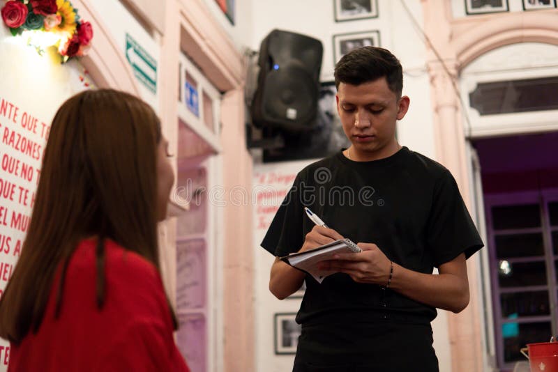 Restaurant waiter dressed in black taking the order from a brown-haired girl dressed in red