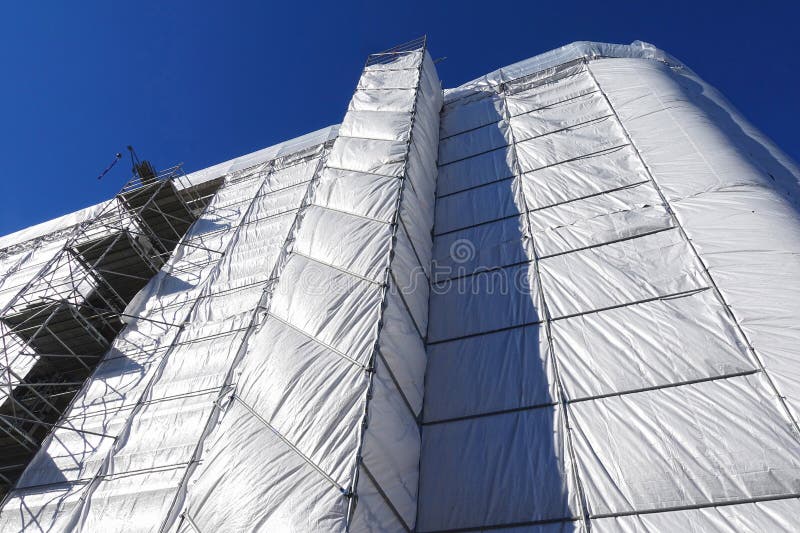 House building, construction, restoration or maintenance site with scaffolding and protective covering of gray tarpaulin. House building, construction, restoration or maintenance site with scaffolding and protective covering of gray tarpaulin