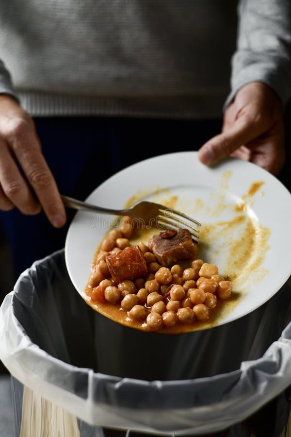 Closeup of a young caucasian man throwing the leftover of a plate of chickpea stew to the trash bin. Closeup of a young caucasian man throwing the leftover of a plate of chickpea stew to the trash bin