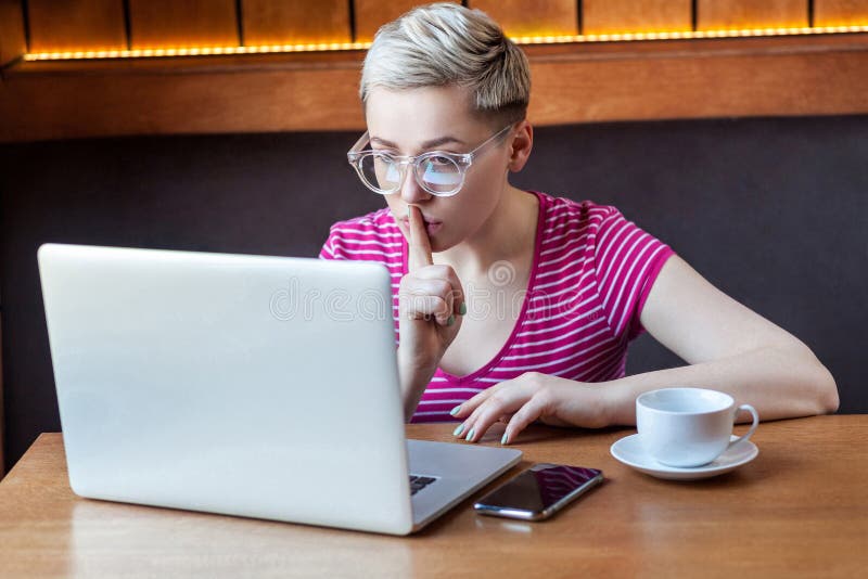 Restez tranquille, s'il vous plaît! Une jeune fille indépendante aux cheveux courts blonds, en chemise rose et lunettes est assi photos stock