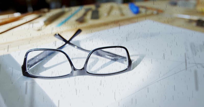 Resting black rectangular eyeglasses open on white paper at workspace, with blurred drawing tools stock photography