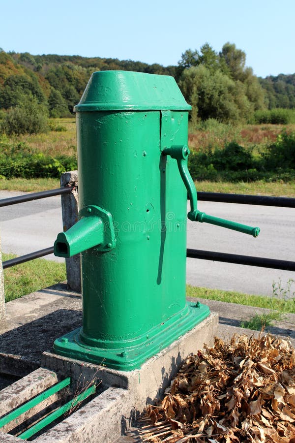 Restored old green outdoor metal water pump with large rotating handle mounted on concrete stand surrounded metal fence and dried stock photo Restored old green outdoor metal water pump with large rotating handle mounted on concrete stand surrounded metal fence and dried stock photo