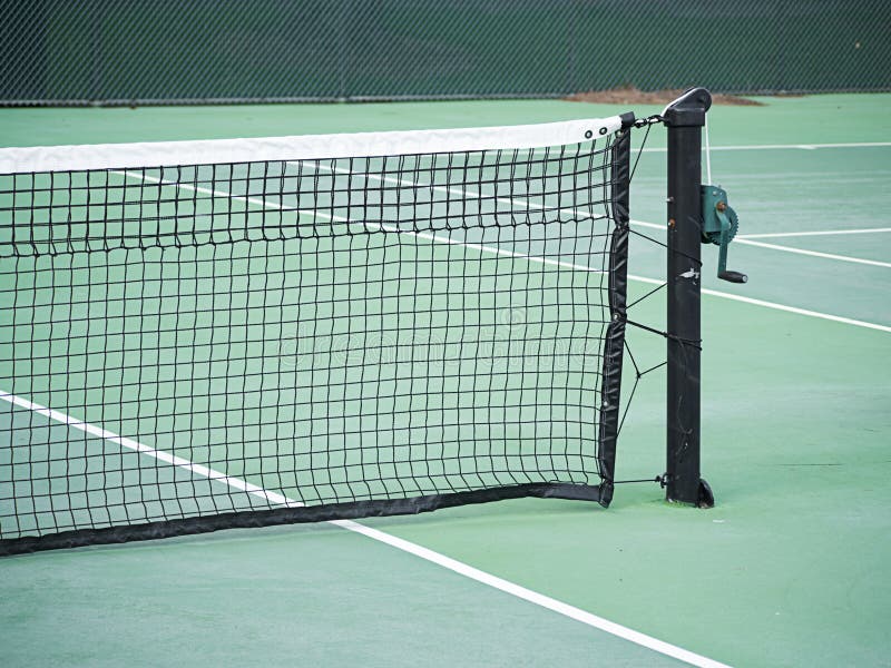 Close-up of tennis net with post and handle on green hard court. Close-up of tennis net with post and handle on green hard court.